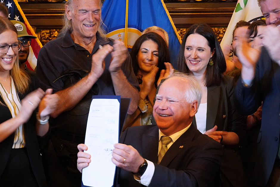Gov. Tim Walz signing the bill to legalize recreational marijuana in the state of Minnesota, surrounded by sponsors and supports, including former Gov. Jesse Ventura.